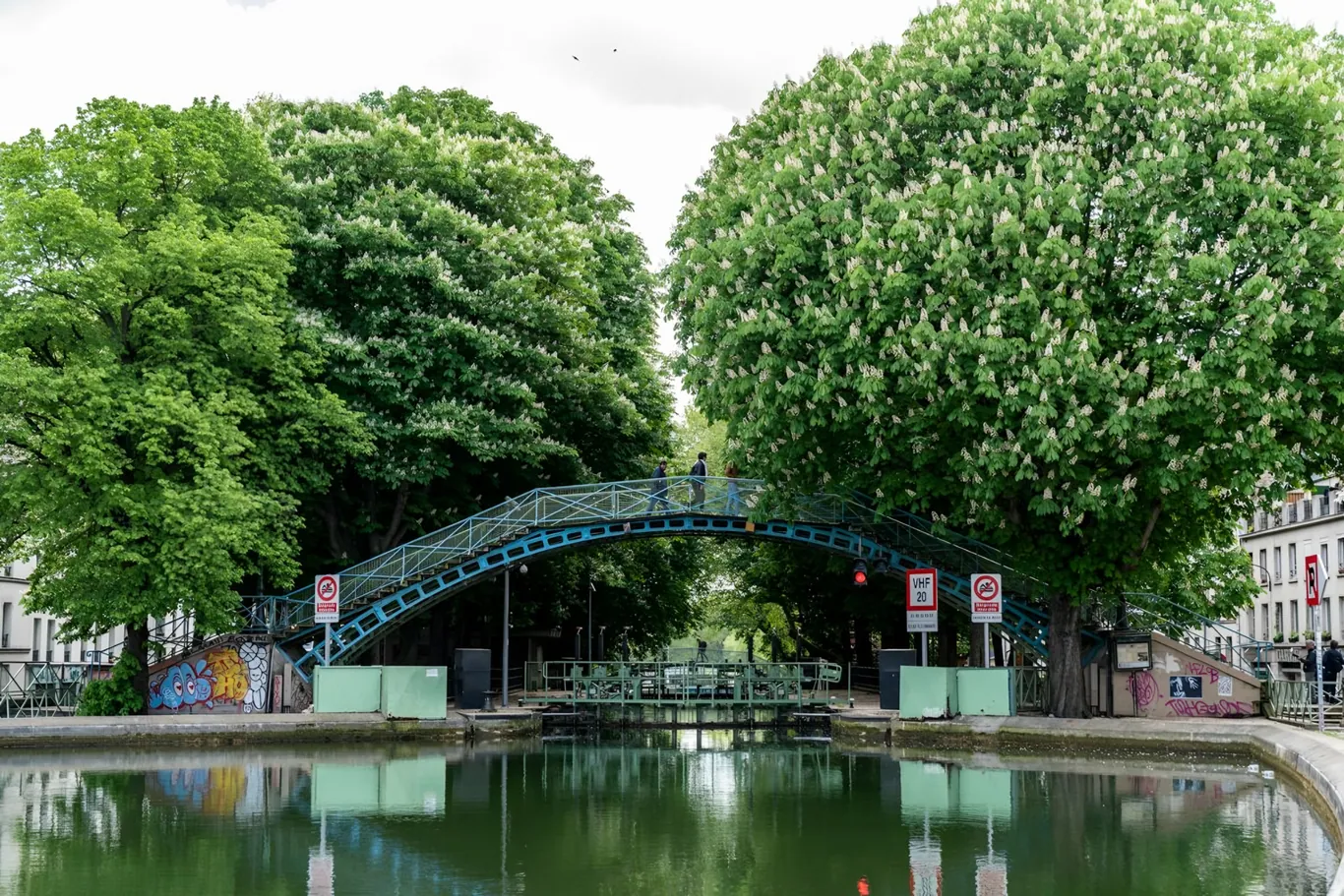 Fietser op de kade langs Canal Saint-Martin met een ijzeren loopbrug op de achtergrond