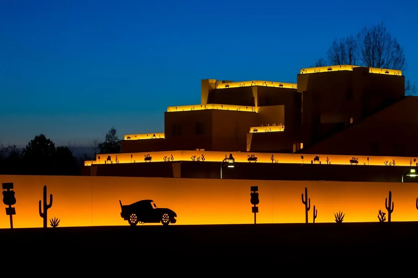 Disney Hotel Santa Fe bij schemer met verlichte muur en silhouet van een auto uit Cars