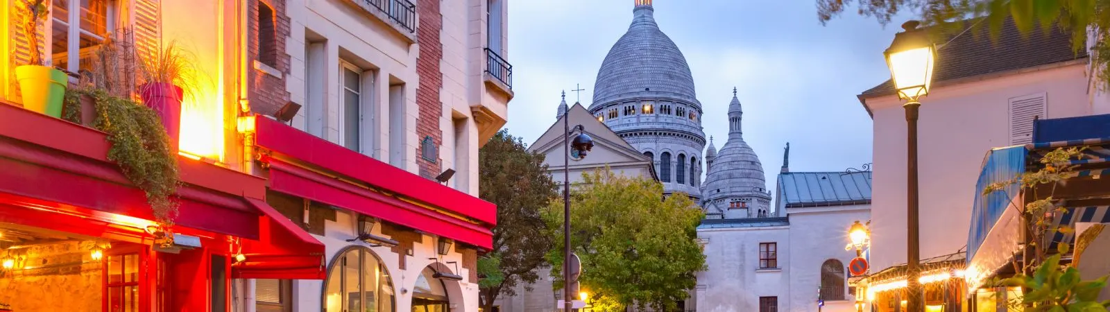 Straat in Montmartre met terrassen en de Sacre-Coeur op de achtergrond in de avondschemering