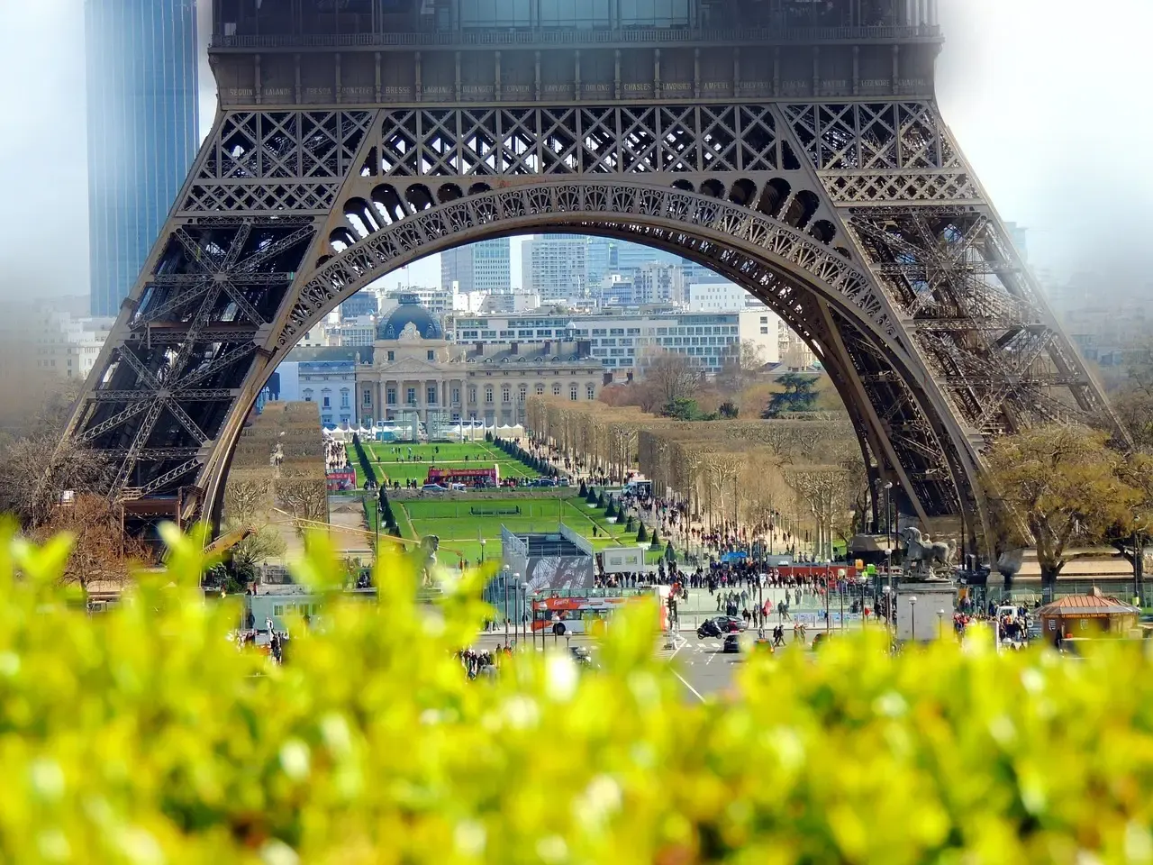 Doorkijk onder de boog van de Eiffeltoren naar de Champ-de-Mars en de Ecole Militaire